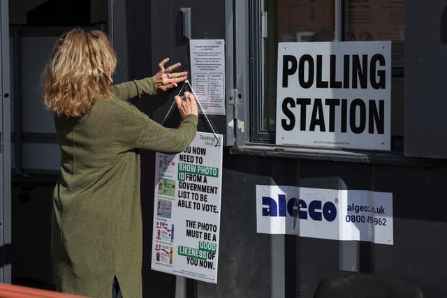 A polling clerk hangs up a sign reminding people to show ID as they turn up to vote in local elections at a mobile polling station in Walton-on-the-Naze, eastern England on May 7, 2026. (AFP)