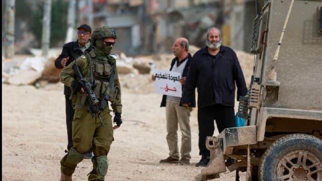 An Israeli soldier walks near Palestinians protesting after Israeli security forces blocked the entrance of the Nur Shams Palestinian refugee camp in the occupied West Bank on February 9, 2026, demanding to be allowed to return to their homes from where t