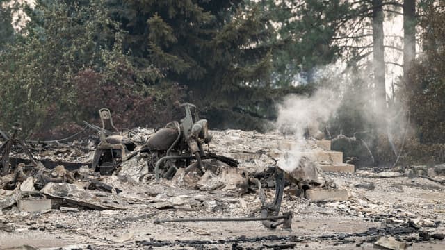 A burned motorcycle sits in the ashes of burned out residential home in the Balboa neighborhood of Spokane, Washington, on August 2, 2026. Fast-moving fires left a trail of destruction in the northwestern US city of Spokane on Sunday, with officials repor