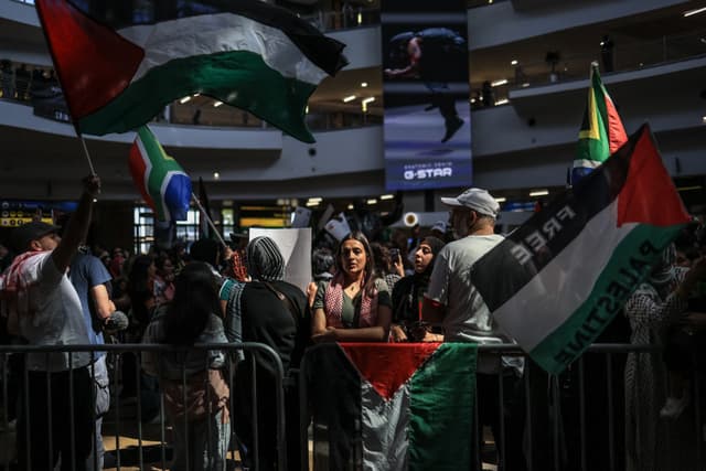 Pro-Palestinian supporters wave flags as they wait for the arrival of South African activists at OR Tambo International Airport in Kempton Park