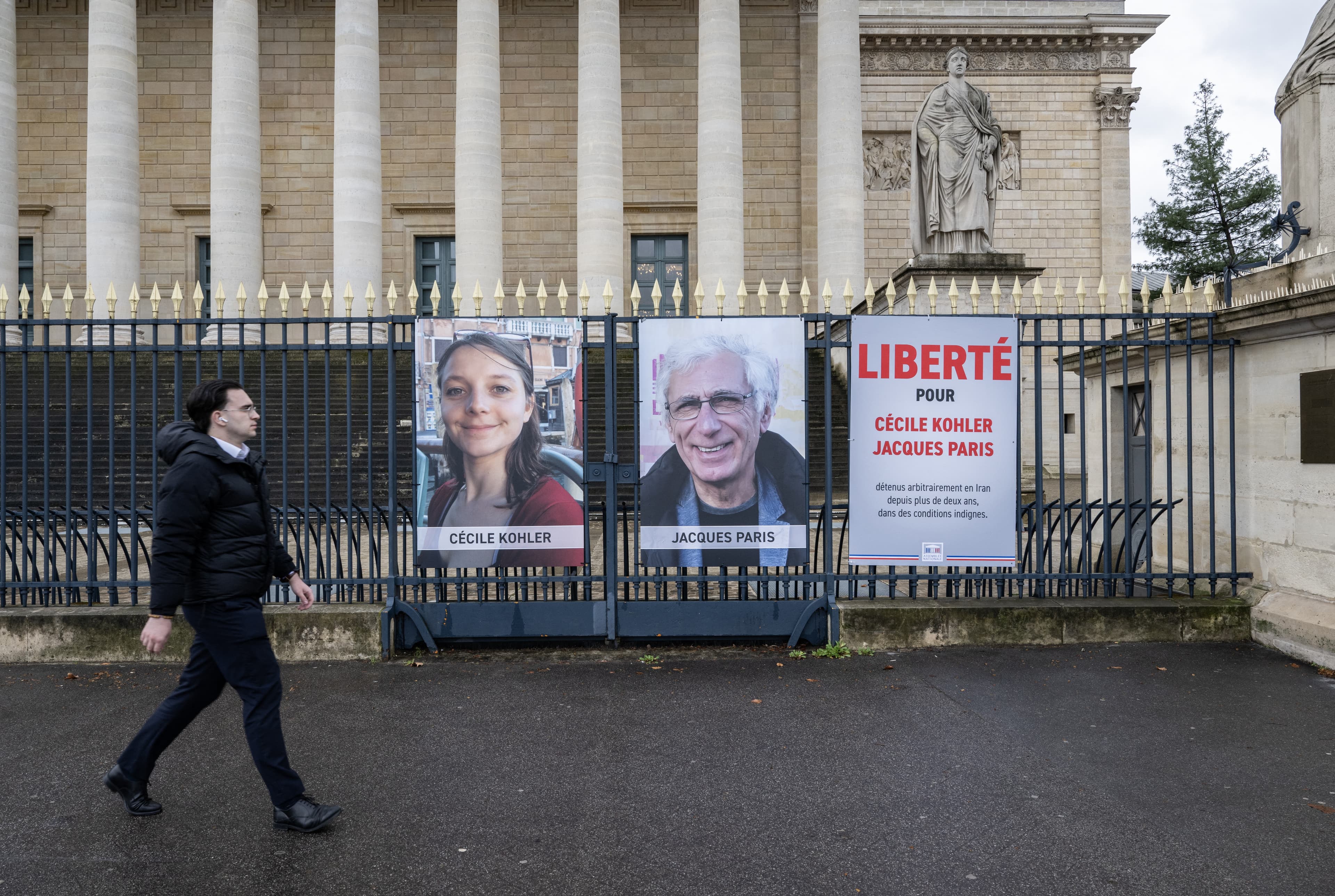 A pedestrian walks past portrait placards of Cecile Kohler and Jacques Paris, two French citizens formerly detained in Iran, set up on a fence of the French National Assembly, in Paris on March 11, 2026. (AFP)