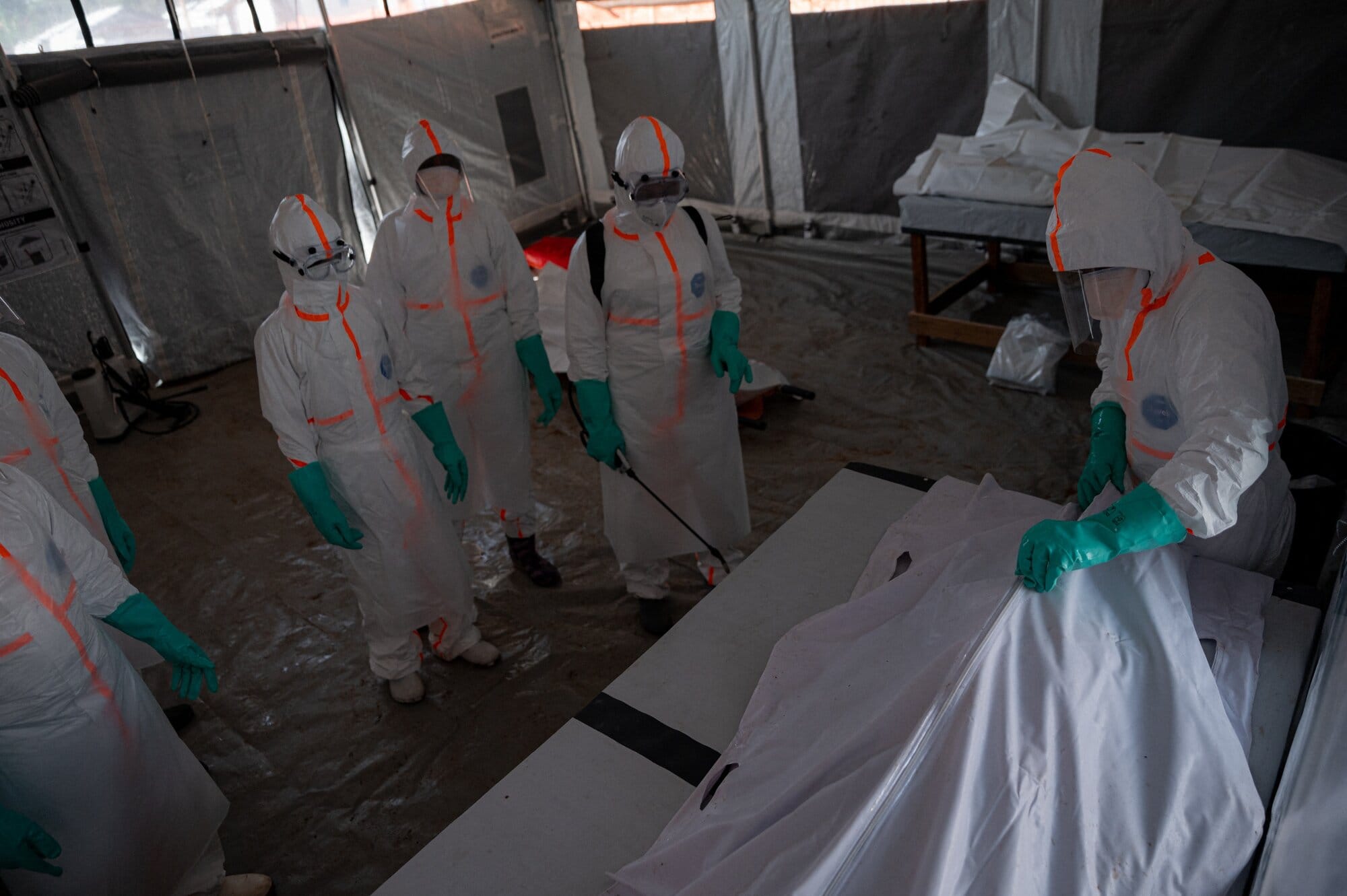 A team of doctors wearing protective suits works in a red zone inside the morgue, close a body bag containing the remains of a man who died from Ebola virus disease on June 13, 2026. (AFP)