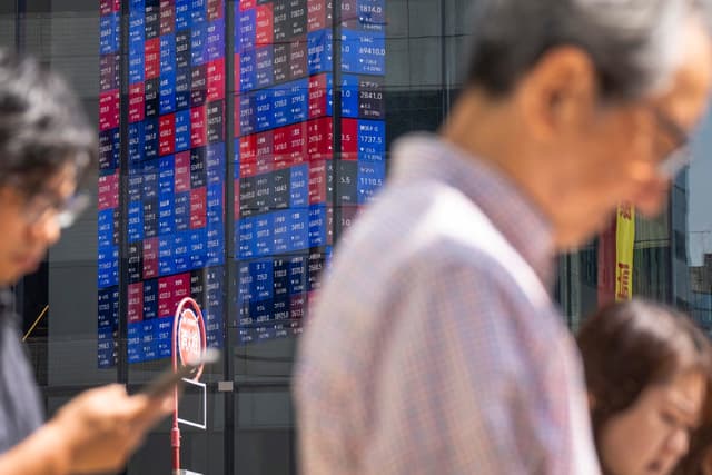 Pedestrians walk past as an electronic quotation board displays the Nikkei 225 stock prices on the Tokyo Stock Exchange in Tokyo on June 16, 2026. (Photo by Kazuhiro NOGI / AFP)
