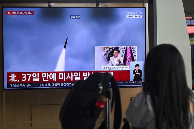 A woman watches a television screen showing a news broadcast with file footage of a North Korean missile test, at a train station in Seoul on May 26, 2026. North Korea launched an "unidentified projectile" into the Yellow Sea off its west coast on May 26,