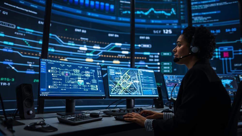 Surveillance specialist working on a computer with a green screen in a room with multiple displays. (AFP)