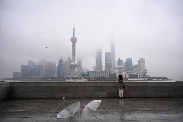 TOPSHOT - A woman takes a photo of the Lujiazui financial district across the Huangpu River on the Bund promenade in Shanghai on March 5, 2026.