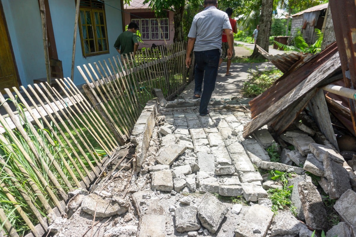 People past damage in a residential area caused by a magnitude 7.8 earthquake off the southern Philippines, at Peta Timur village in Sangihe Islands Regency, Indonesia's North Sulawesi province on June 8, 2026.