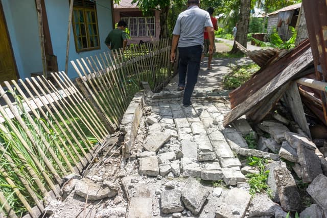 People past damage in a residential area caused by a magnitude 7.8 earthquake off the southern Philippines, at Peta Timur village in Sangihe Islands Regency, Indonesia's North Sulawesi province on June 8, 2026.