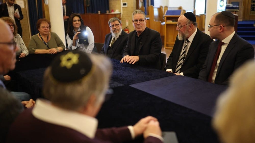 Britain's Prime Minister Keir Starmer (C) and Chief Rabbi Ephraim Mirvis (2R) sit alongside Kenton Rabbi, Yehuda Black (4L) talks during a visit to Kenton United Synagogue, which was recently the target of an attempted arson, in the Kenton district of Lon