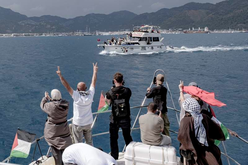 People raise V-signs and take photos from a boat decorated with Palestinian flags as another vessel displaying solidarity signs sails past near the port in Marmaris, Turkey, on May 14, 2026. (AFP)