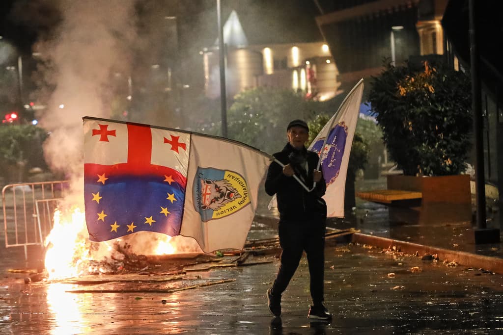 A demonstrator with a Georgian national, EU and other flags walks in front of police line during an opposition rally in the city center of Tbilisi, Georgia, on Saturday, Oct. 4, 2025, boycotting the municipal elections and calling for the release of polit