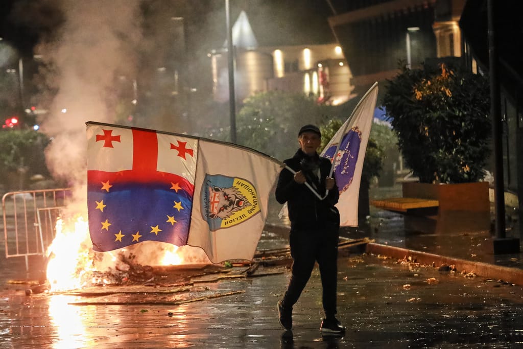 A demonstrator with a Georgian national, EU and other flags walks in front of police line during an opposition rally in the city center of Tbilisi, Georgia, on Saturday, Oct. 4, 2025, boycotting the municipal elections and calling for the release of polit