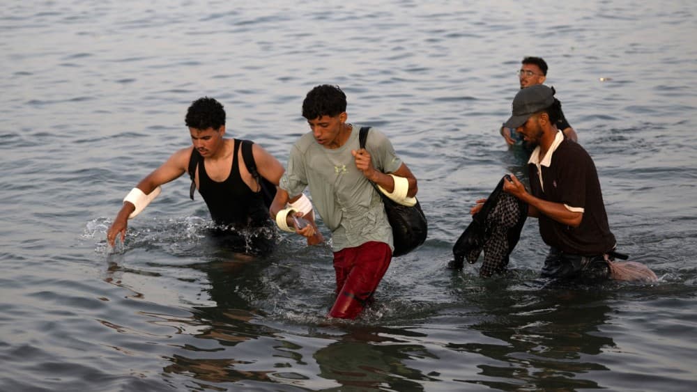 Migrants wade through the water near the border with Morocco as they attempt to enter Spain's North African enclave of Ceuta on July 31, 2026 (AFP)