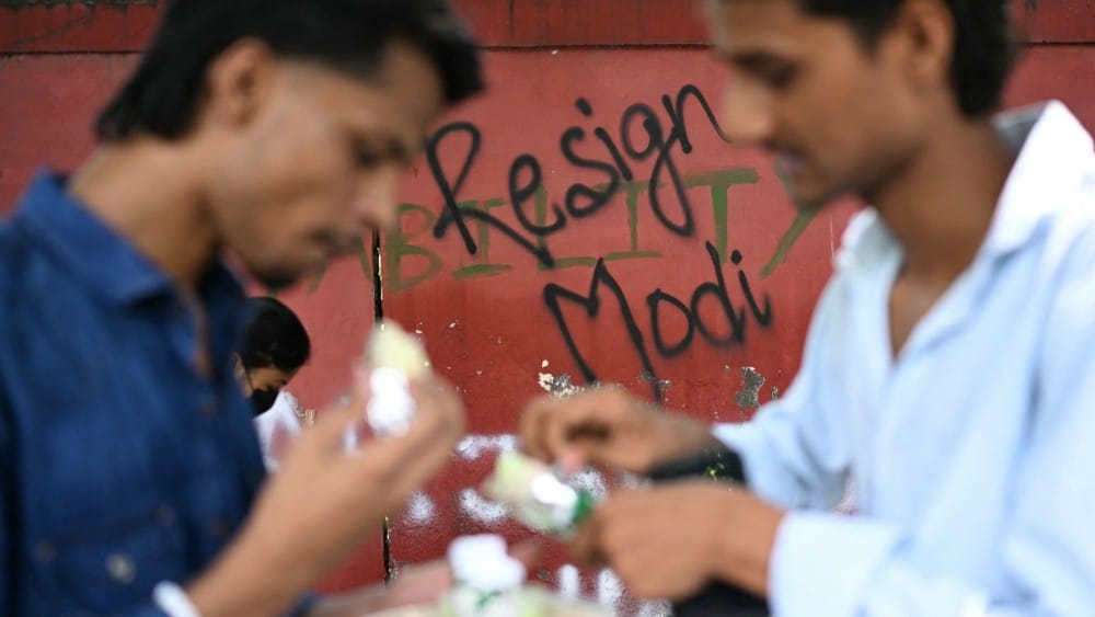 Cockroach Janta Party (CJP) supporters eat near a wall mural at Jantar Mantar in New Delhi on July 22, 2026 during the ongoing protest to demand the resignation of India's Education Minister Dharmendra Pradhan over alleged NEET exam irregularities. (Photo