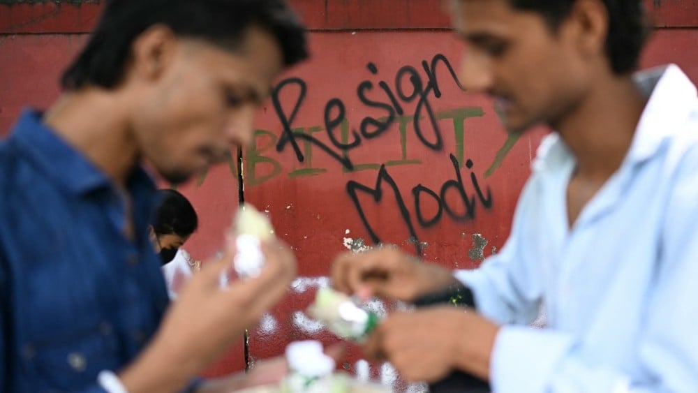 Cockroach Janta Party (CJP) supporters eat near a wall mural at Jantar Mantar in New Delhi on July 22, 2026 during the ongoing protest to demand the resignation of India's Education Minister Dharmendra Pradhan over alleged NEET exam irregularities. (Photo