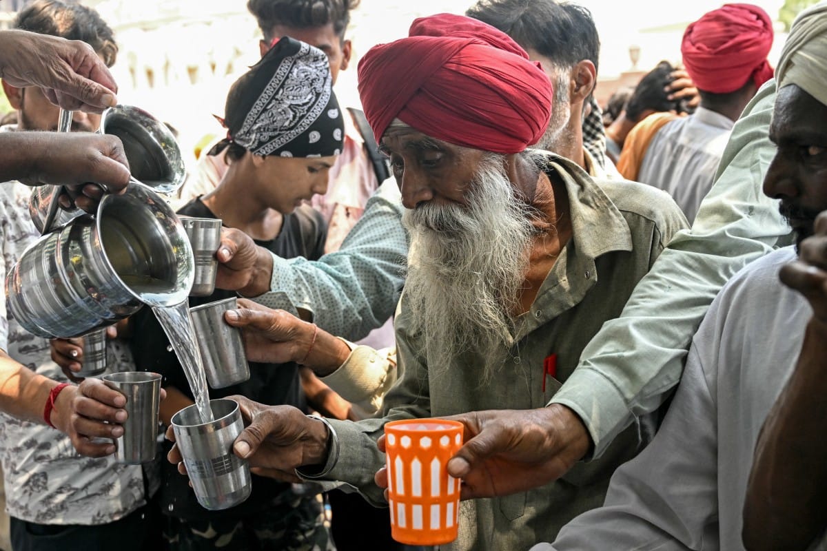 People drink sweetened water distributed by volunteers along a street on a hot summer day in Amritsar on June 4, 2026. (Photo by Narinder NANU / AFP)