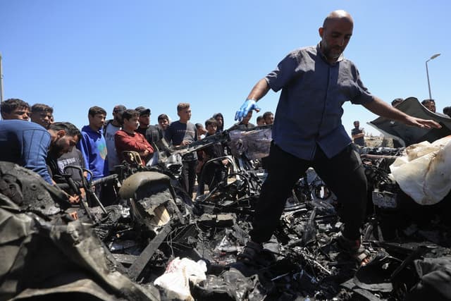 People inspect a destroyed civilian vehicle after it was targeted by an Israeli airstrike that reportedly killed three people on Salah al-Din Street, south of Bureij camp for Palestinian refugees in the central Gaza Strip on April 23, 2026. (AFP)